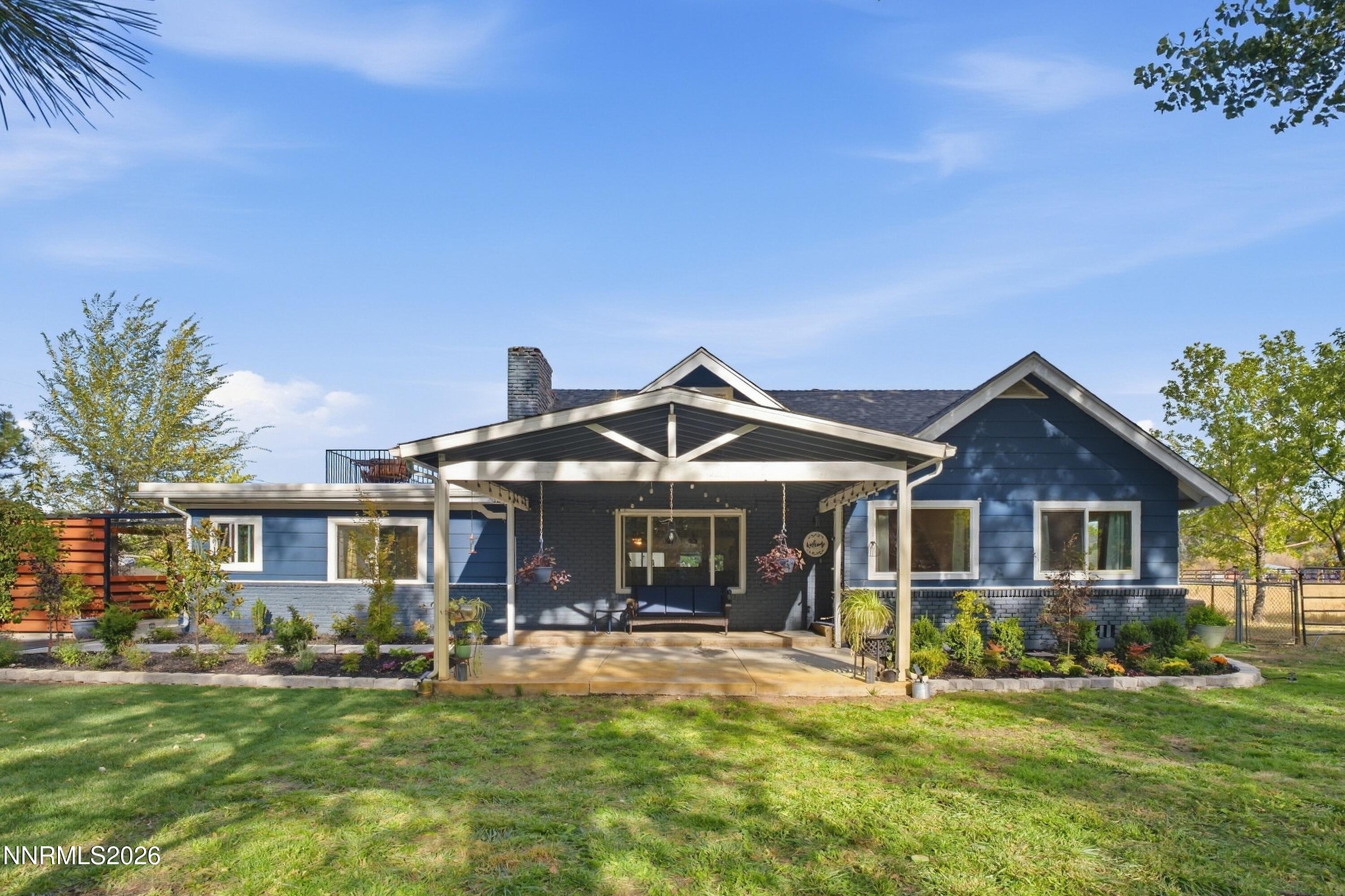 Blue house with a covered backyard patio, hanging planters, and a landscaped lawn.