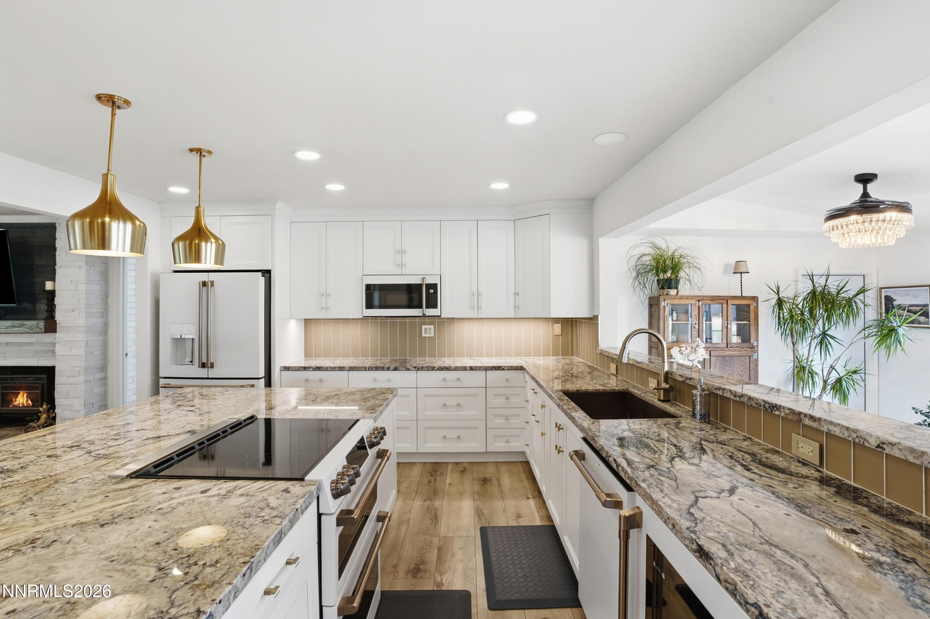 Bright kitchen with granite counters, white cabinetry, brass pendants, and a large cooktop island.