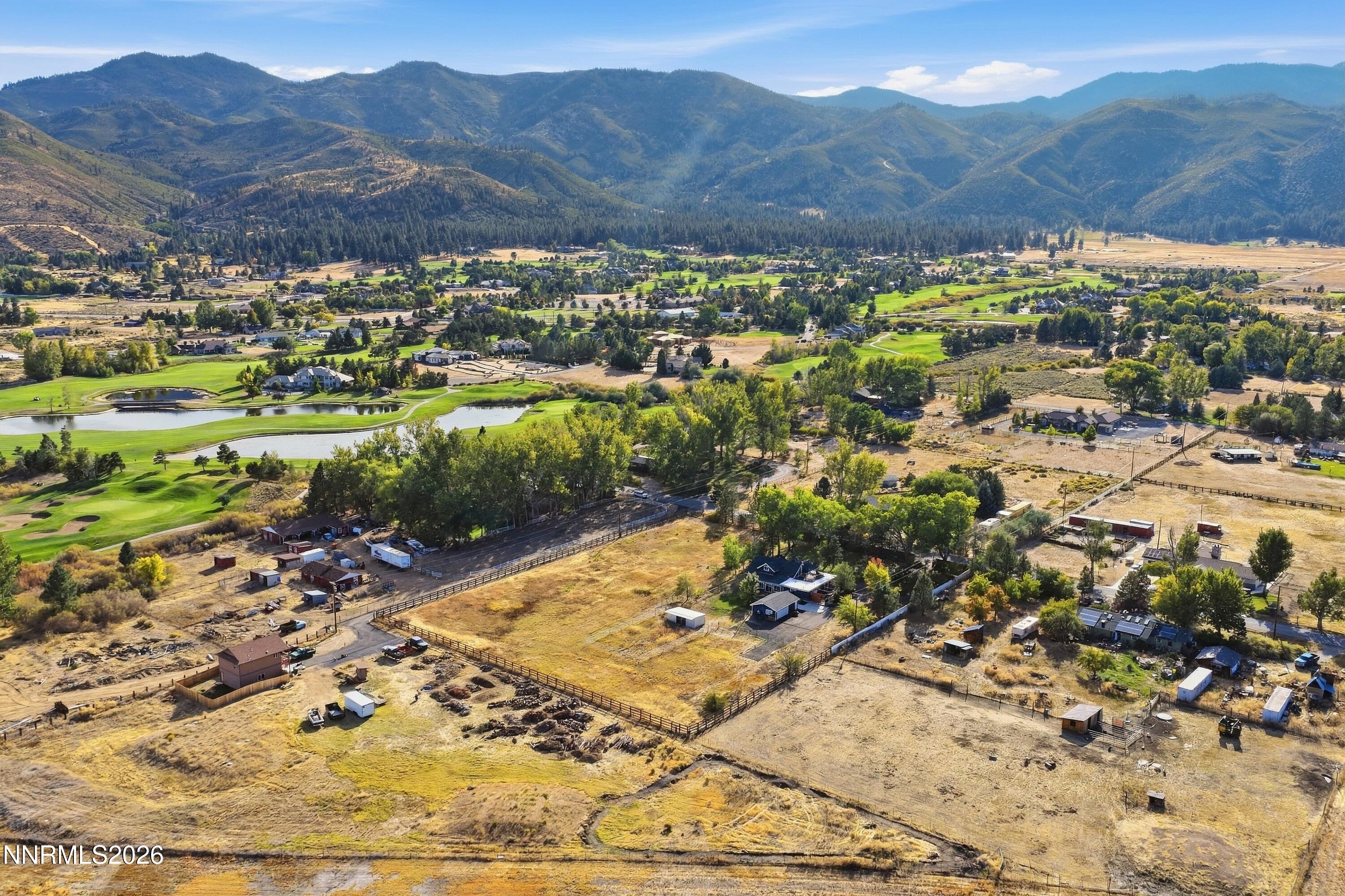 Aerial view of rural acreage, a golf course, and forested mountains across the valley.