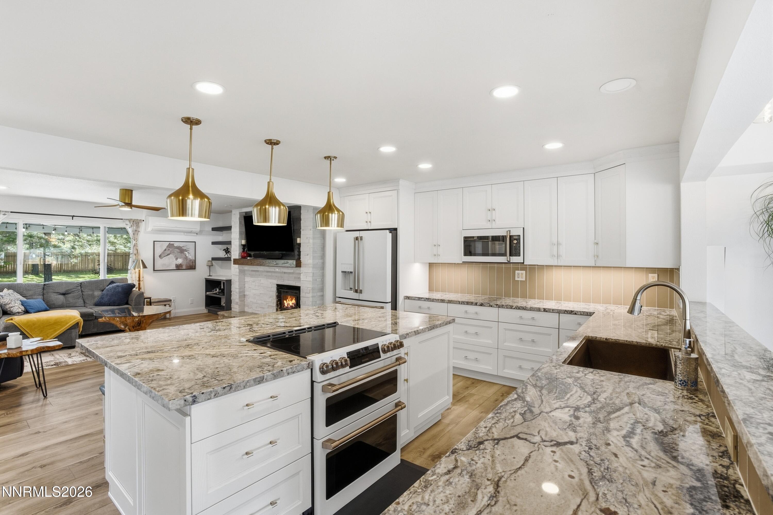 Renovated white kitchen with a large stone island, brass pendant lights, and an adjoining living room.
