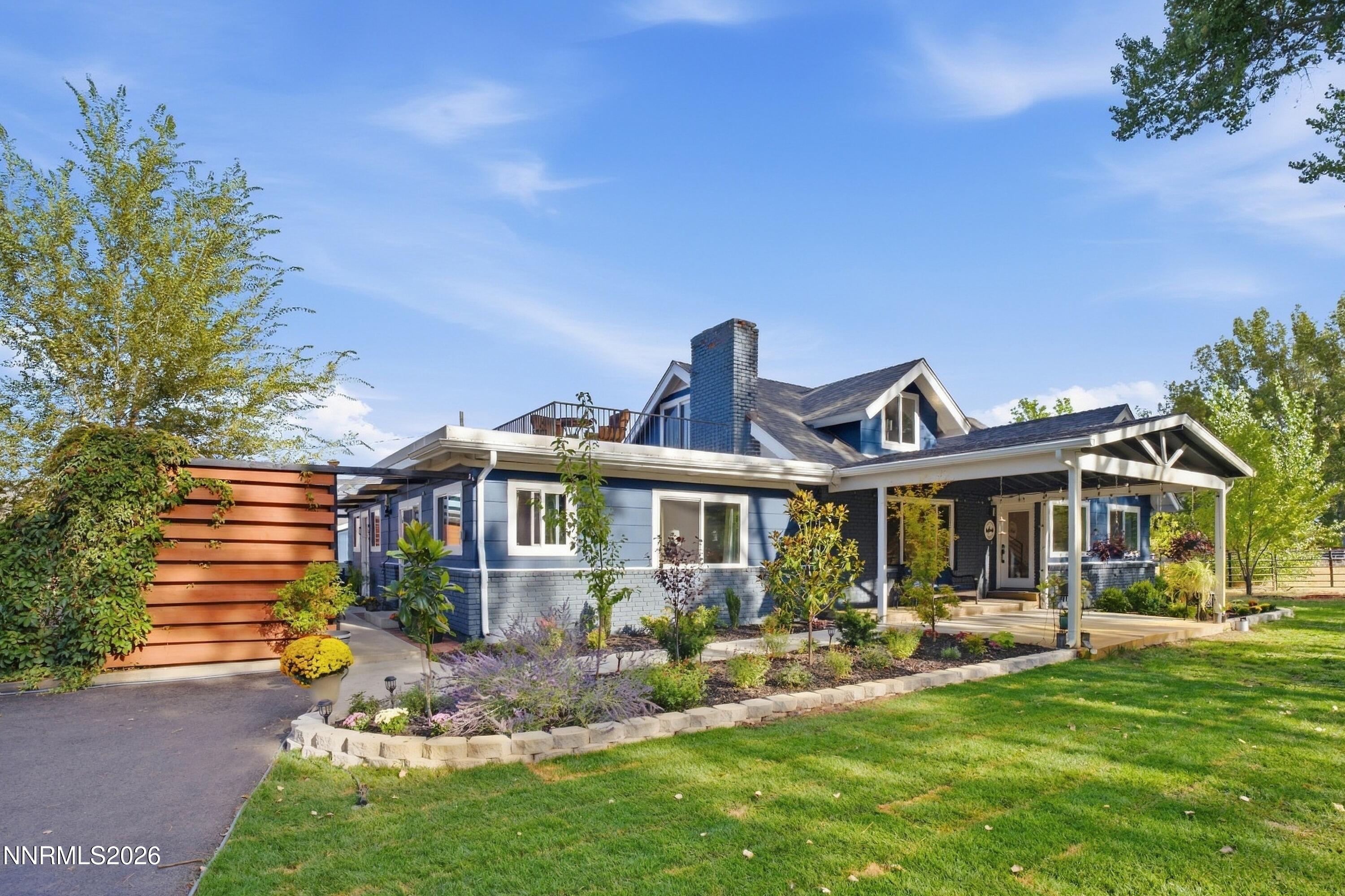 Blue-sided home with a covered porch, rooftop deck, and landscaped front lawn.