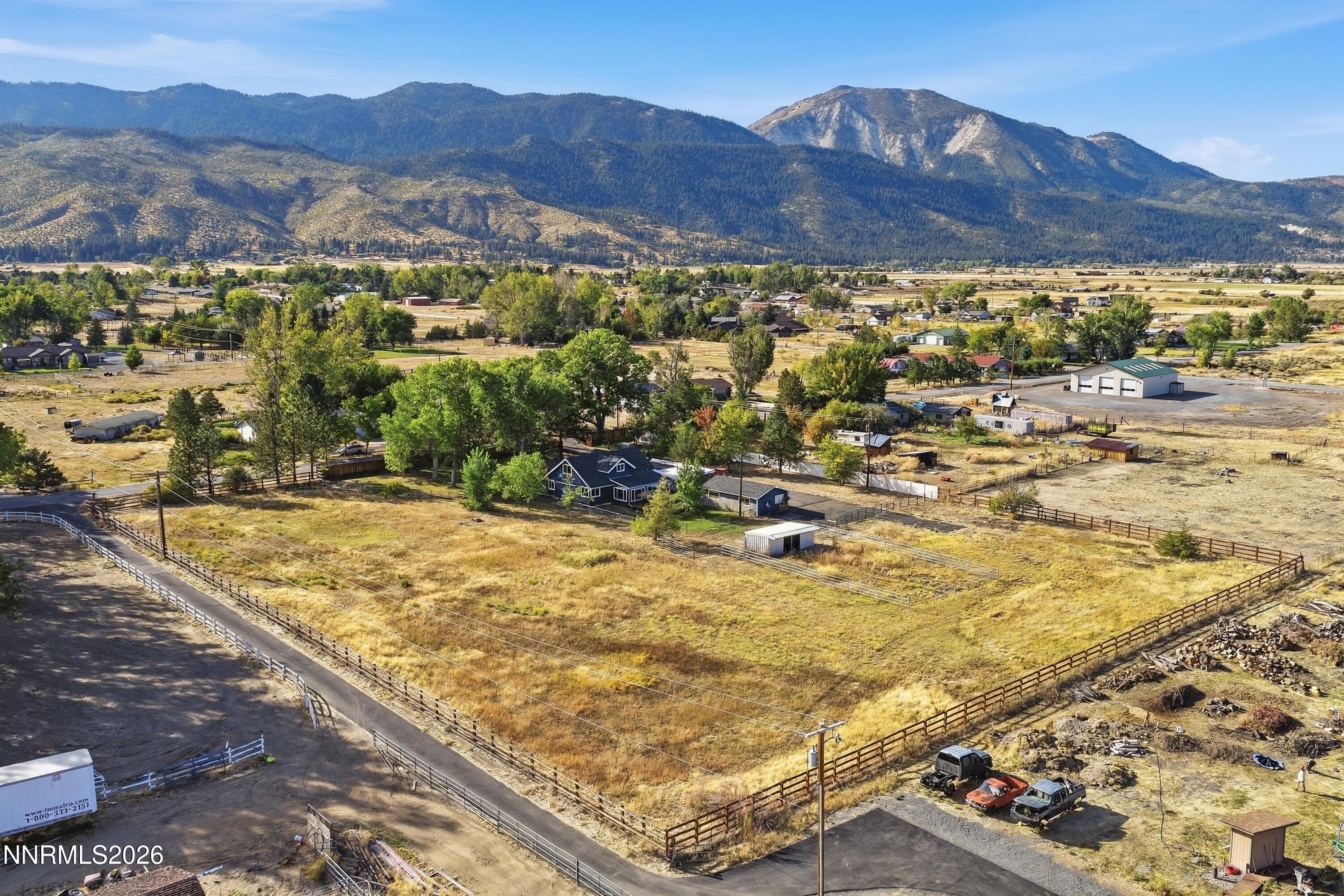 Aerial view of a fenced rural property with a dark house and mountain views.