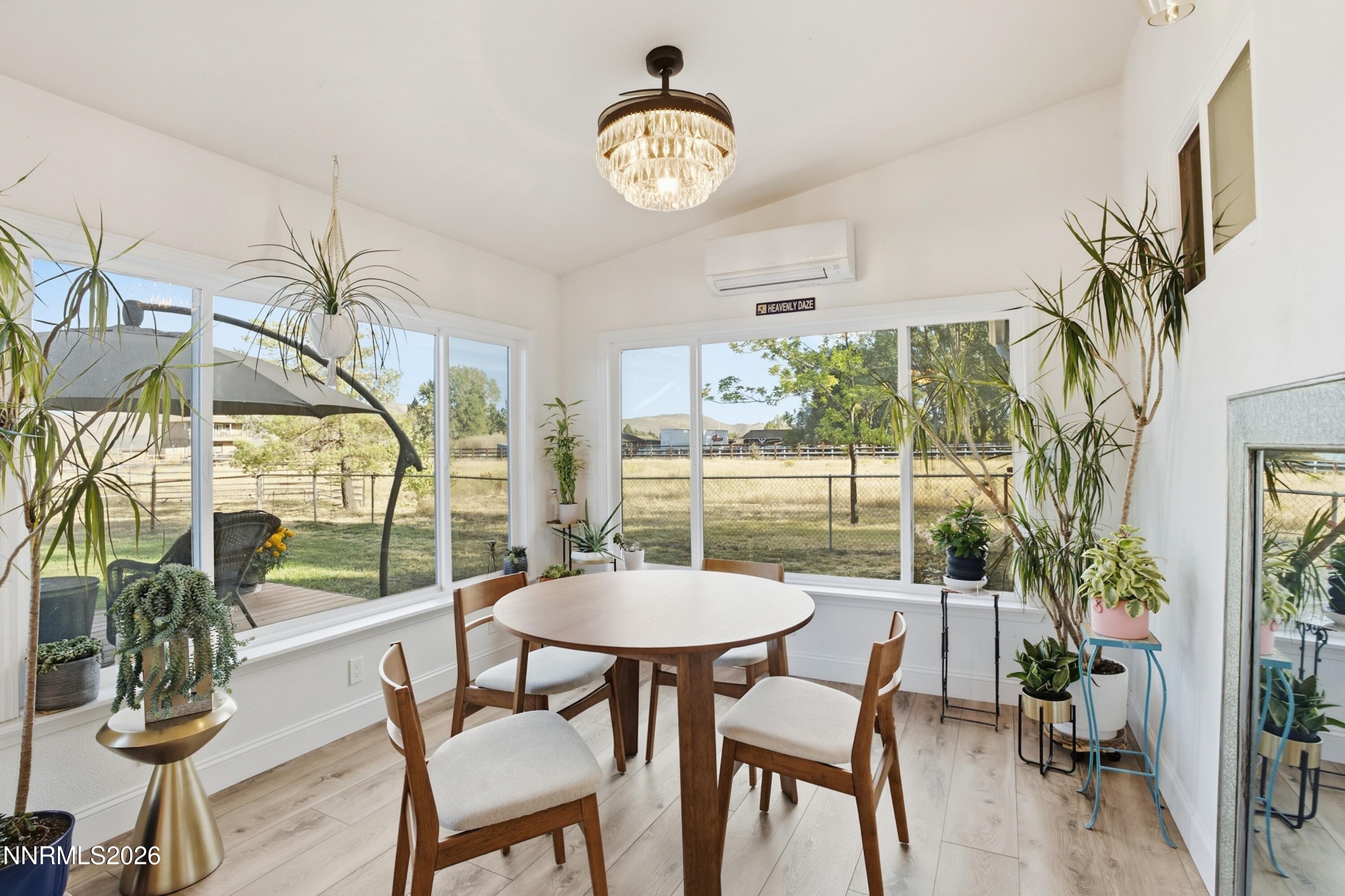 Dining room with a round wooden table, large windows, and views of a fenced yard.