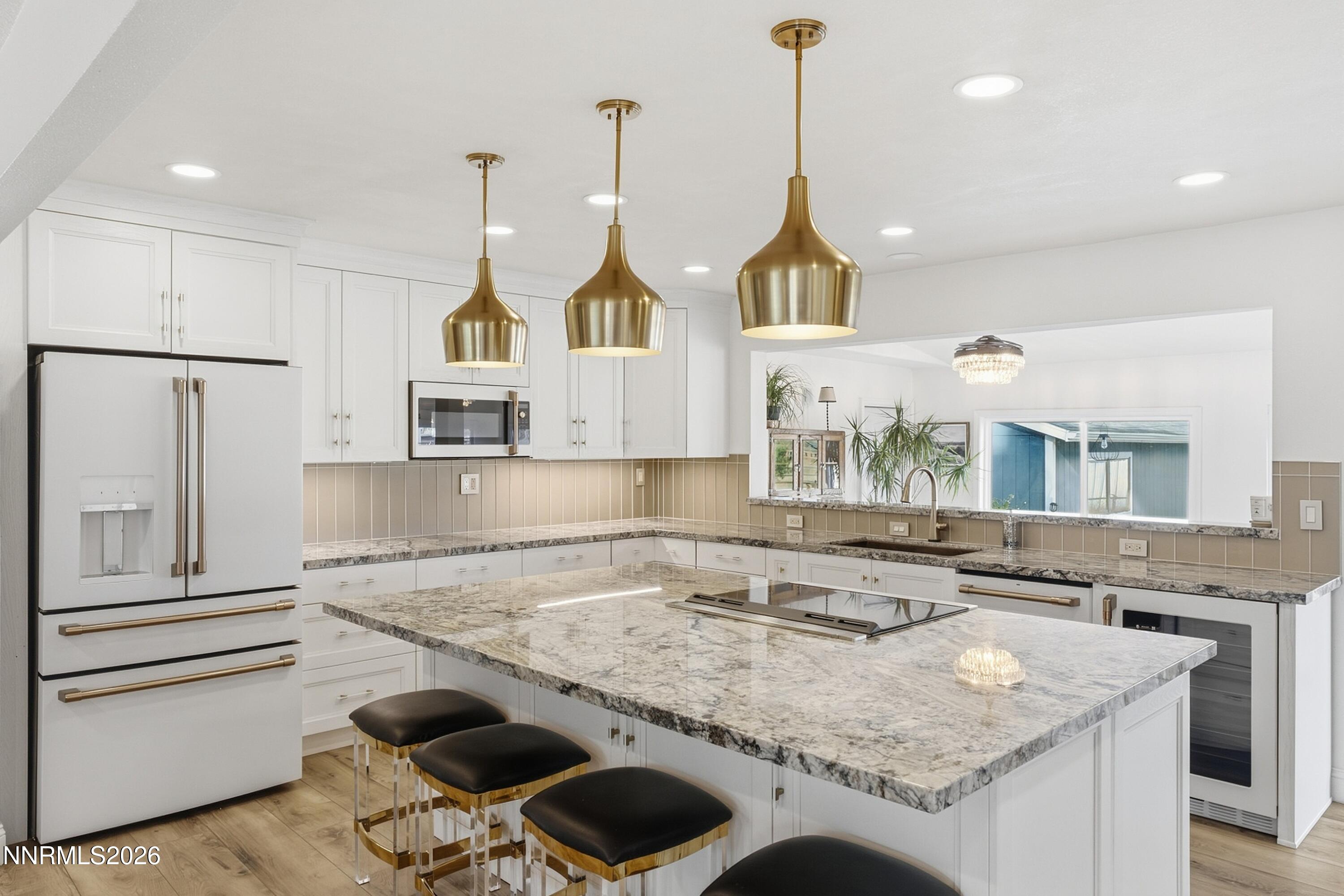 Remodeled white kitchen with a large stone island, brass pendant lights, and stainless steel appliances.