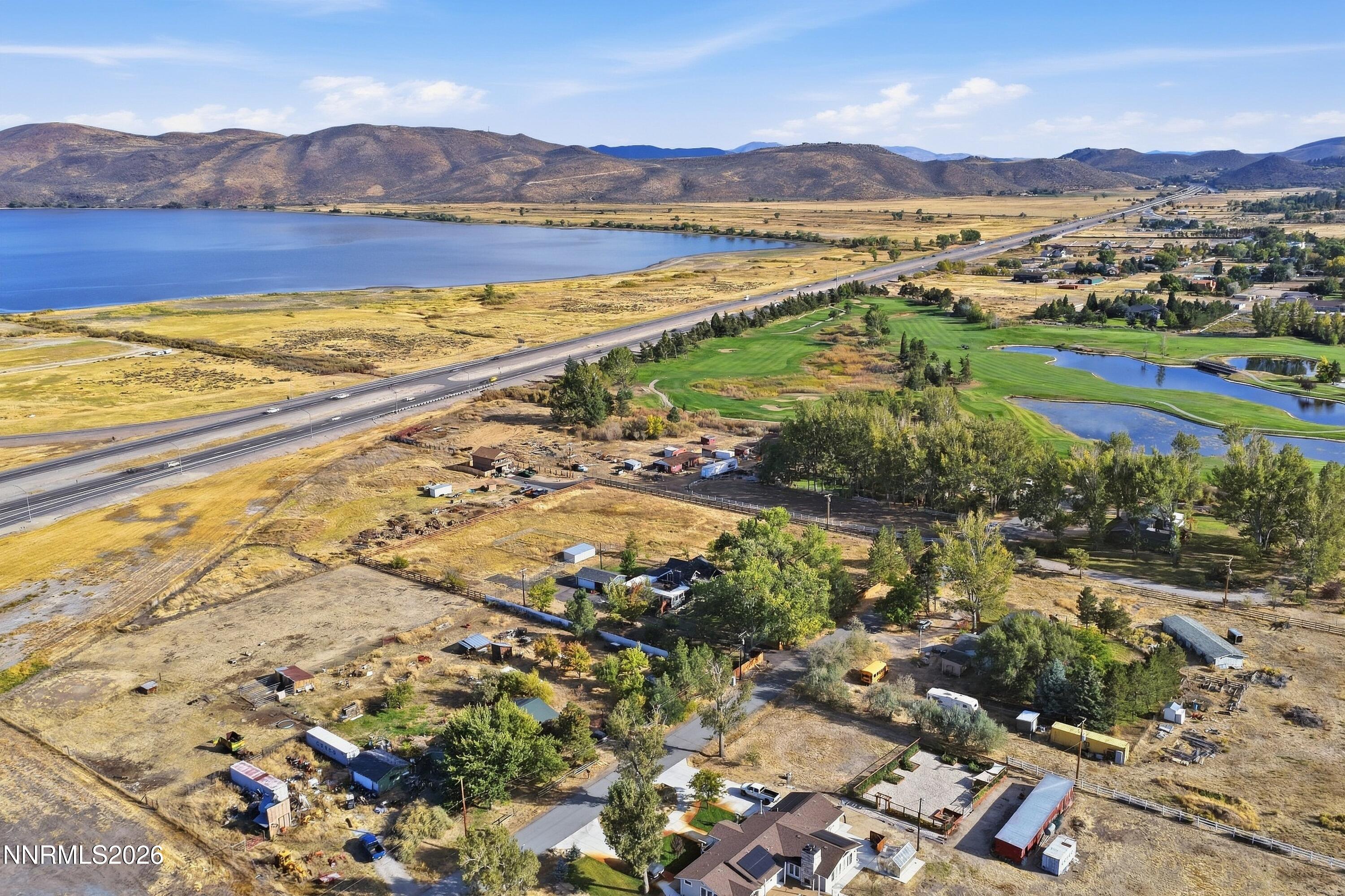 Aerial view of rural properties beside a lake and golf course, with mountains beyond.