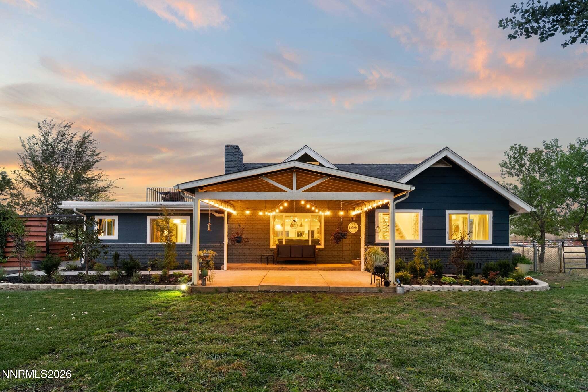 Dark blue house with a covered, string-lit patio and landscaped lawn at dusk.