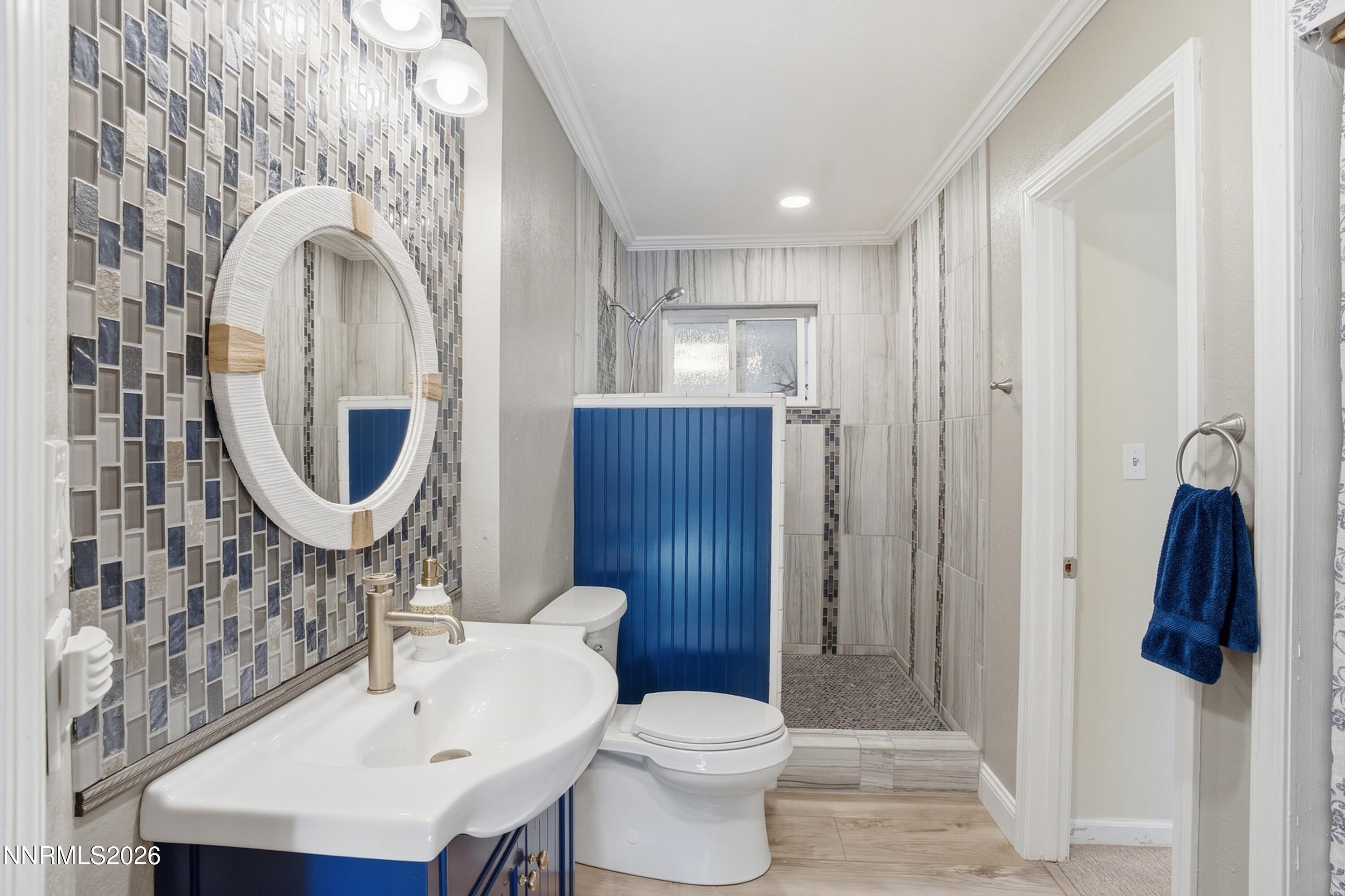 Bathroom with a blue vanity and shower panel, mosaic tile wall, and oval mirror.