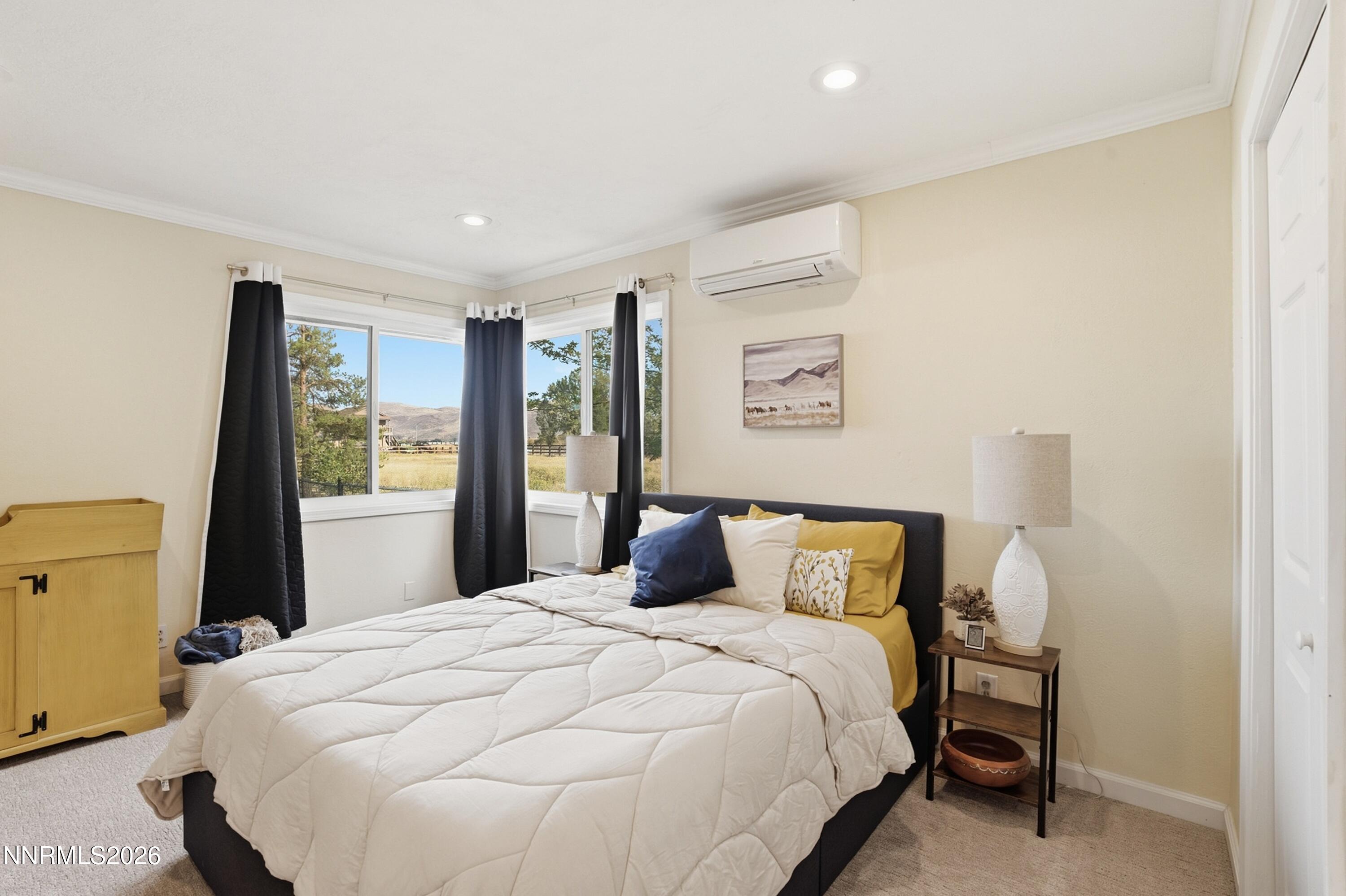 Staged bedroom with a white bed, dark curtains, and corner windows overlooking open land and hills.