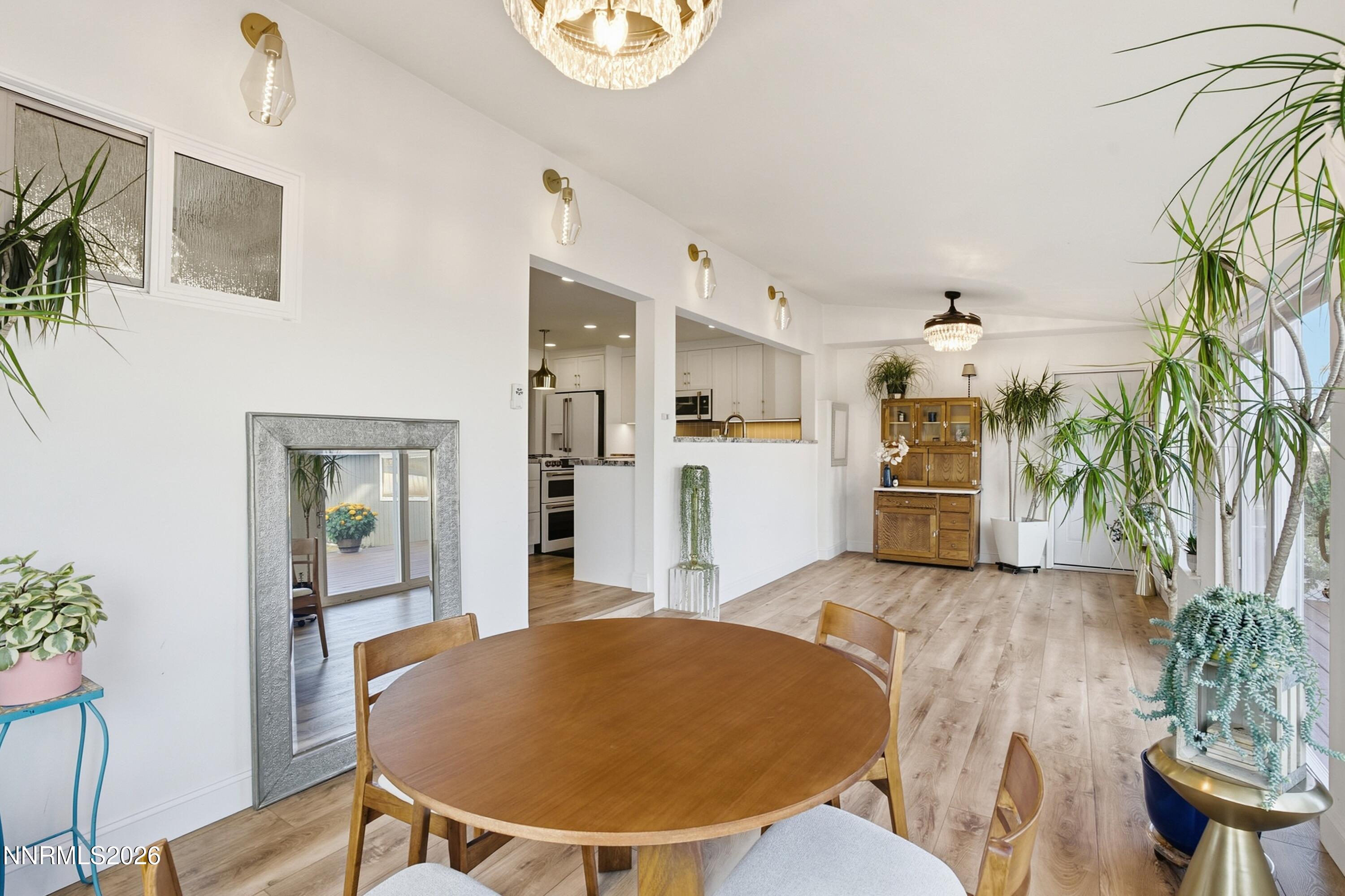 Dining area with a round wooden table, tall plants, and an open view into the kitchen.