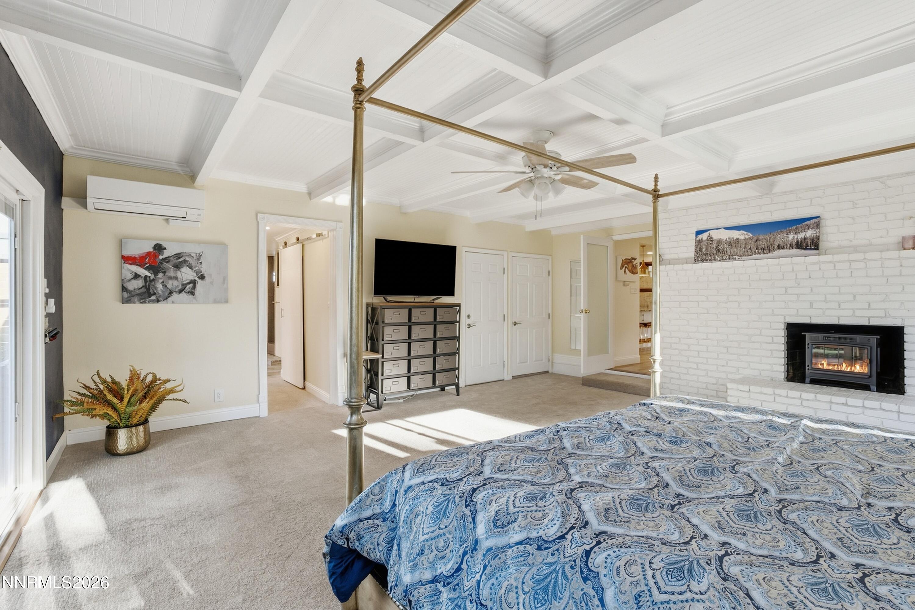 Bedroom with a blue patterned bedspread, brass four-poster frame, coffered ceiling, and white brick fireplace.