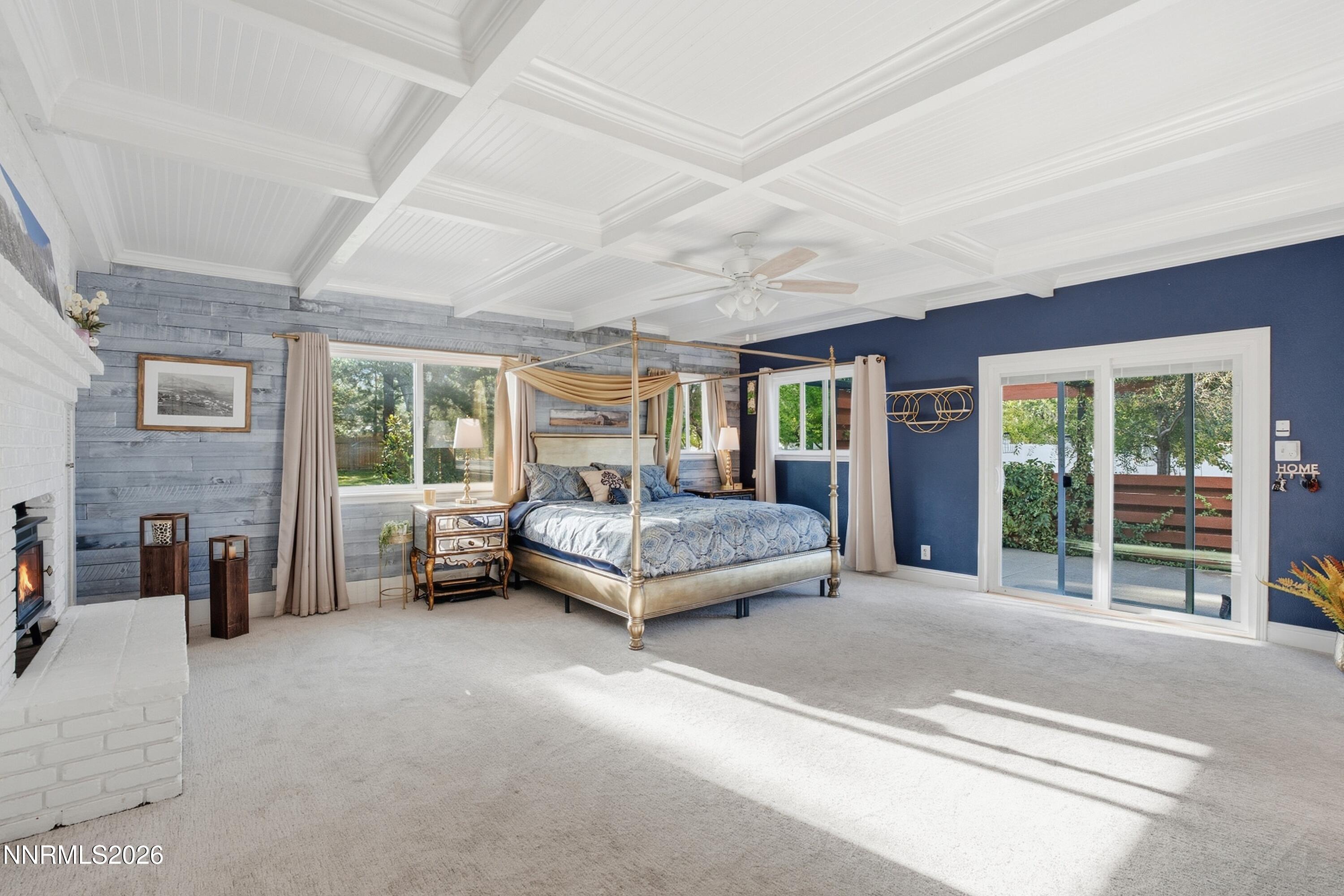 Bedroom with a canopy bed, white brick fireplace, coffered ceiling, and sliding patio doors.