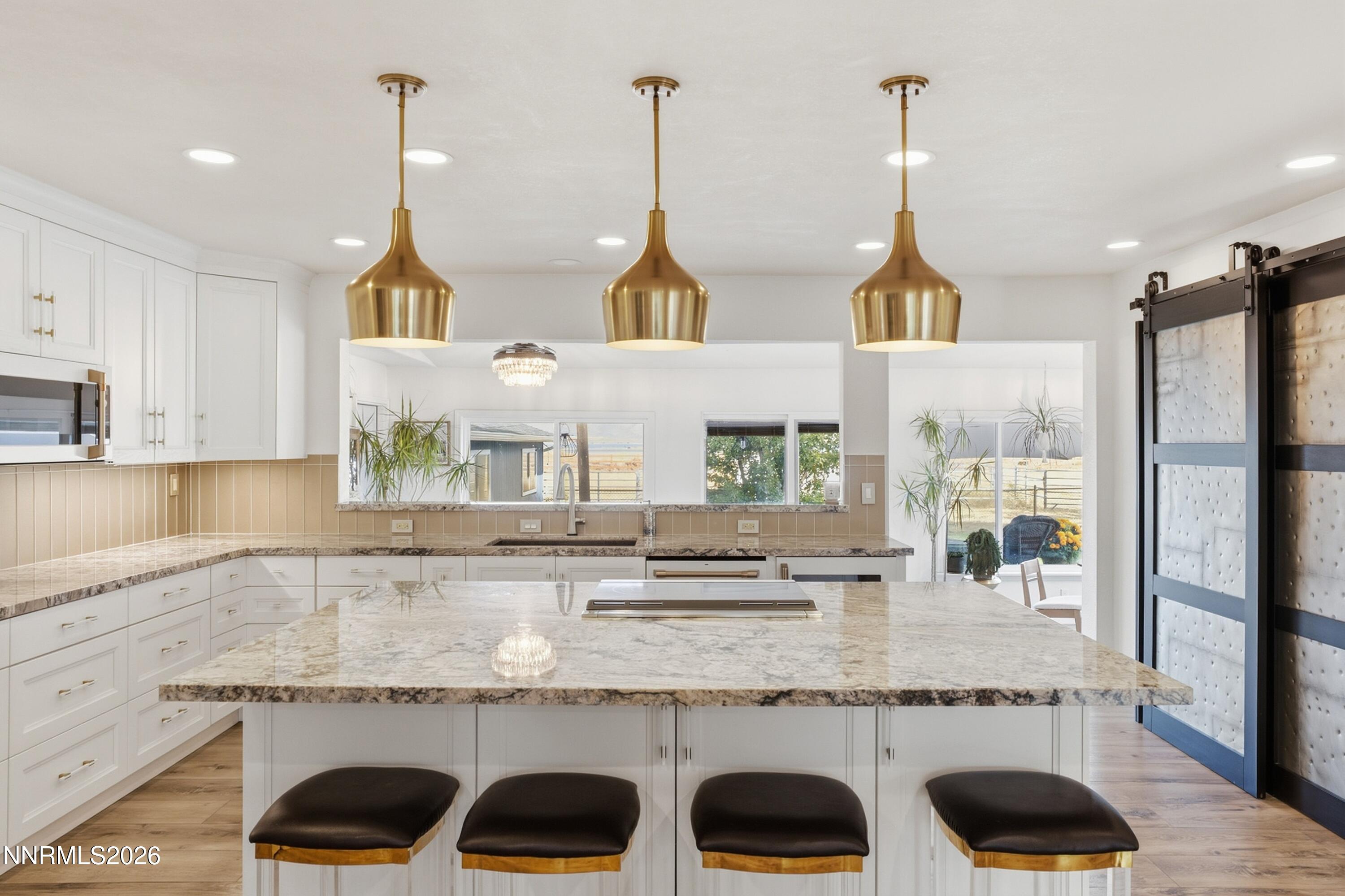 Bright white kitchen with a marble island, four stools, brass pendants, and a sliding barn-style door.