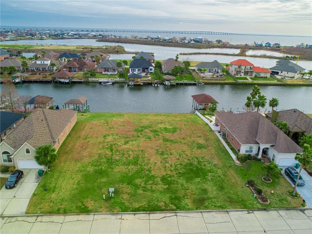 Vacant waterfront lot with a grassy yard, canal frontage, and homes across the water.