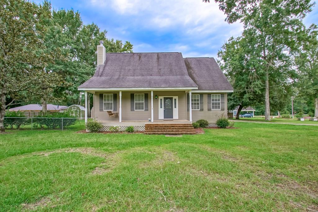 One-story beige house with a covered porch and brick steps, set on a broad lawn beneath mature trees.