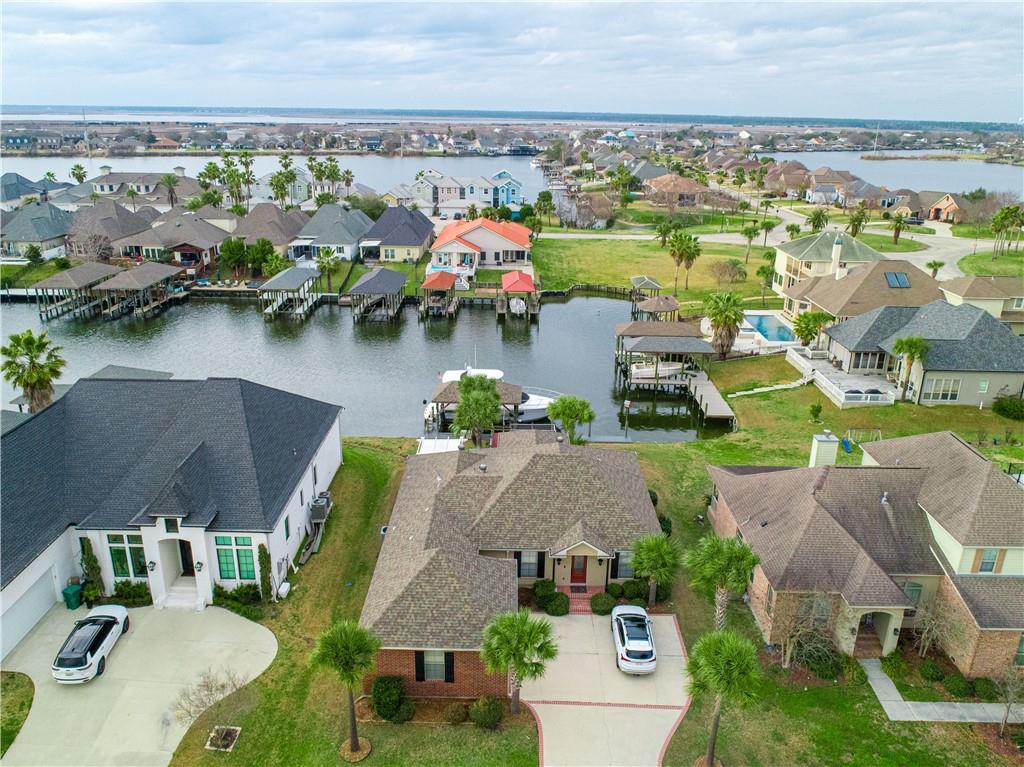 Aerial view of waterfront homes and docks along a canal, with palm trees and water beyond.