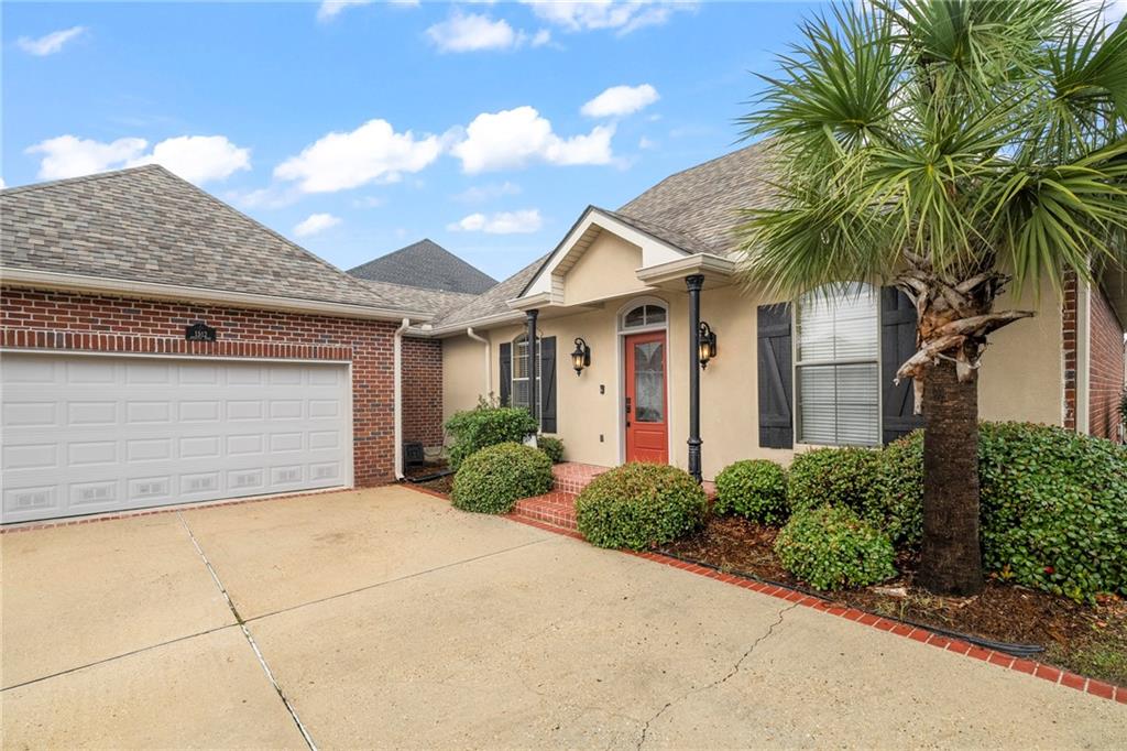 Home exterior with a two-car garage, red front door, landscaped shrubs, and a palm tree.