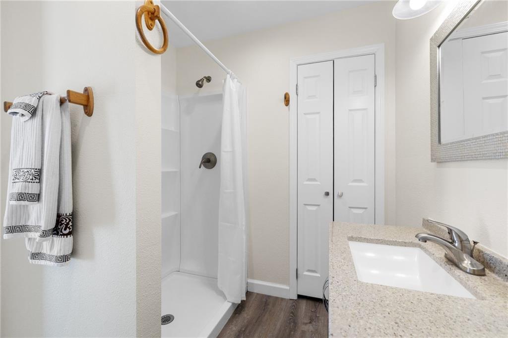 Bathroom with a white shower, speckled vanity countertop, mirrored cabinet, and dark wood-look floor.