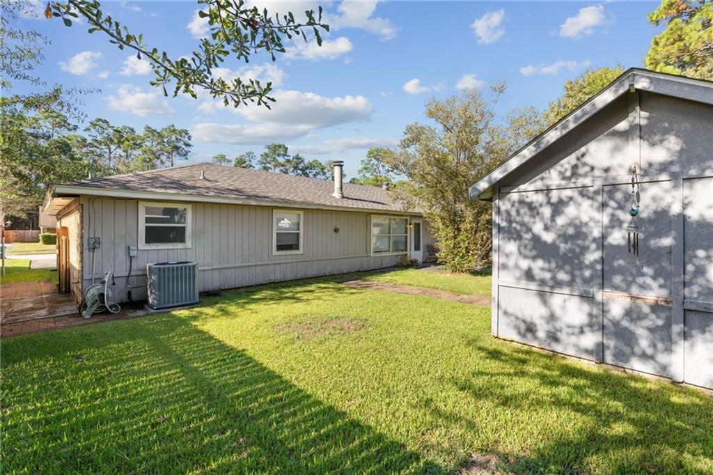 Rear exterior of a single-story gray home beside a matching shed with a green lawn.
