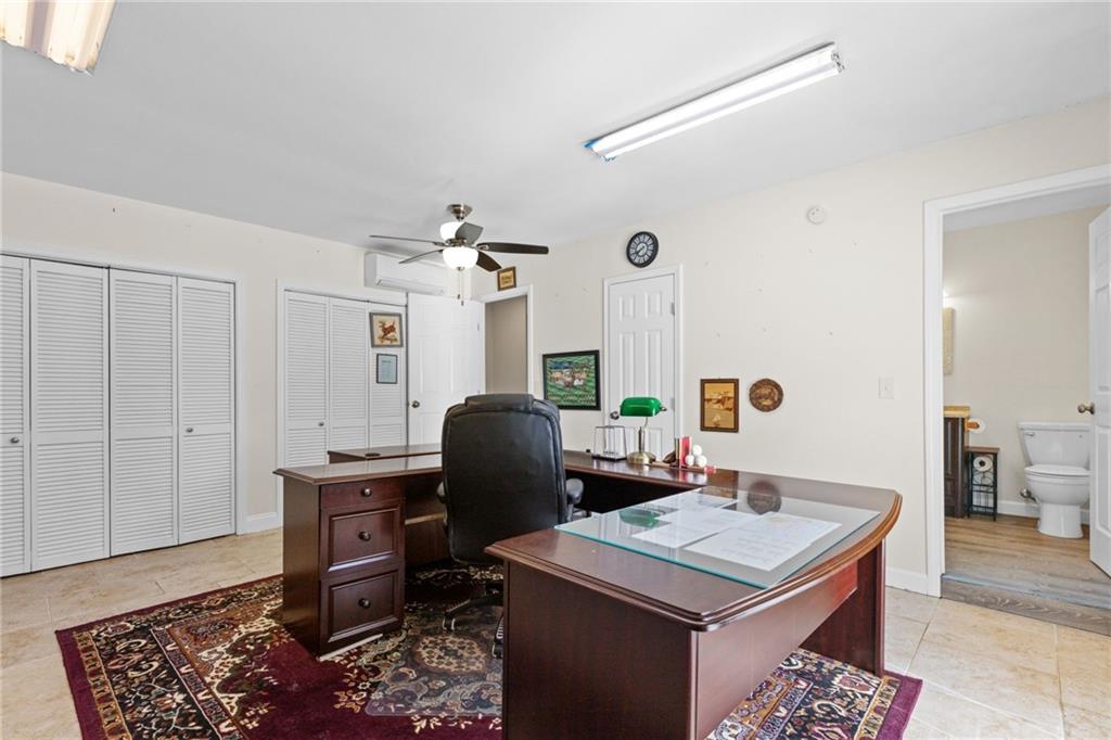 Furnished office with dark wood desks, a black chair, and white louvered closet doors.