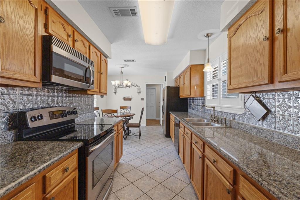 Kitchen with honey-colored cabinets, granite counters, stainless appliances, and patterned metal backsplash.