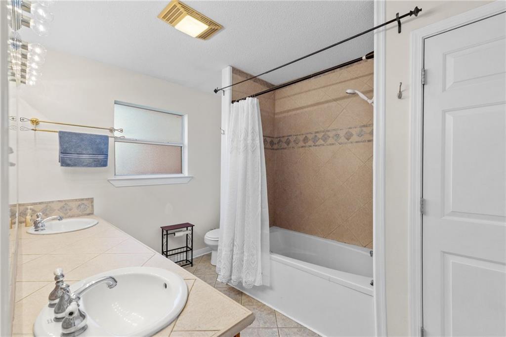 Bathroom with a double-sink vanity and bathtub with tan tile surround.