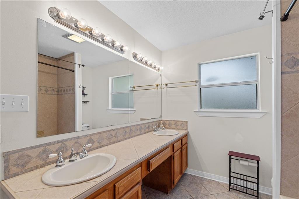Bathroom with a long double-sink vanity, wood cabinets, and a large wall mirror.