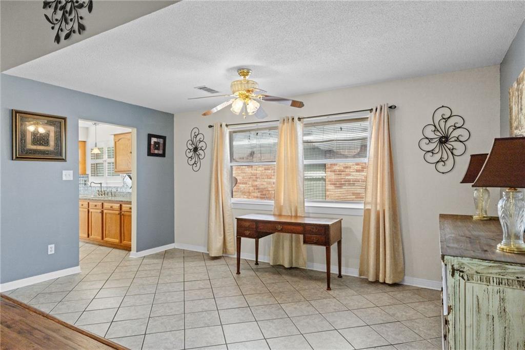 Dining area with tiled floors, curtained windows, and a wooden desk beside the kitchen doorway.