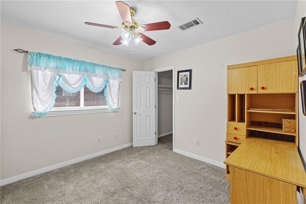 Carpeted room with a wooden built-in desk, ceiling fan, and window with turquoise curtains.