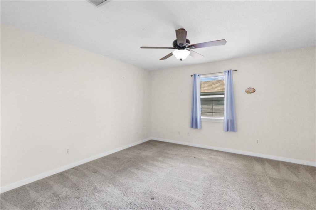 Empty bedroom with gray carpet, a ceiling fan, and a window framed by blue curtains.