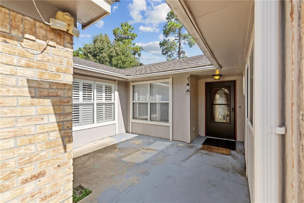 Covered front entry courtyard with a concrete patio, shuttered windows, and a dark glass-paneled door.