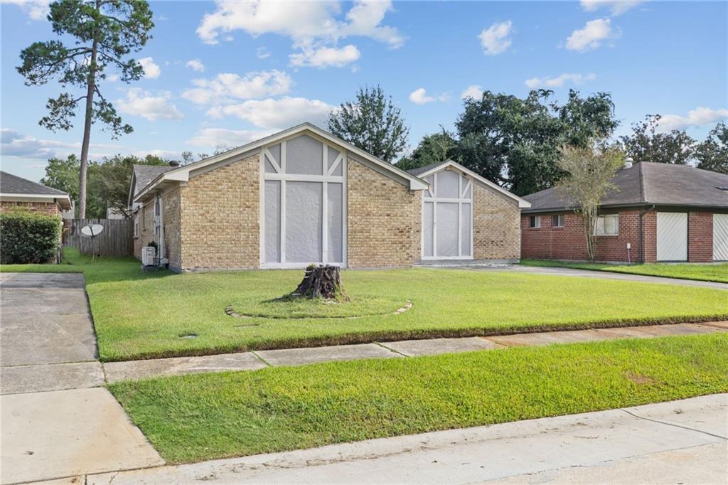 Single-story tan brick home with white gable trim and a broad green front lawn.