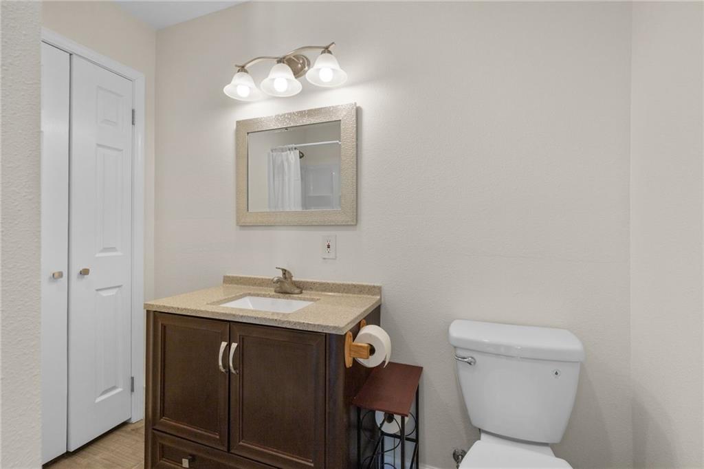 Bathroom with a dark wood vanity, beige countertop, framed mirror, and white toilet.