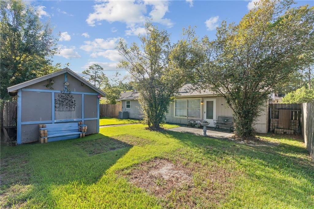 Fenced backyard with a single-story home, blue garden shed, and patio seating beneath mature trees.