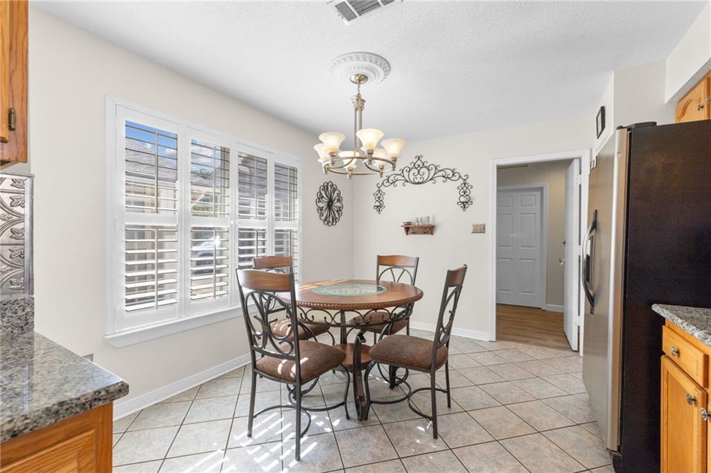 Kitchen dining area with a round table beneath a chandelier and wide plantation-shuttered windows.