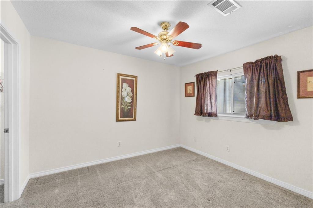 Empty carpeted bedroom with a ceiling fan and a curtained window.