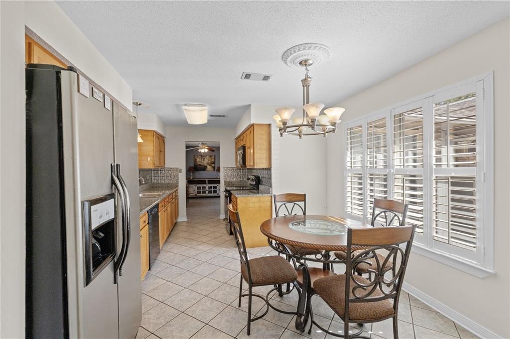 Kitchen and dining area with honey-colored cabinets, stainless steel refrigerator, and shuttered windows.
