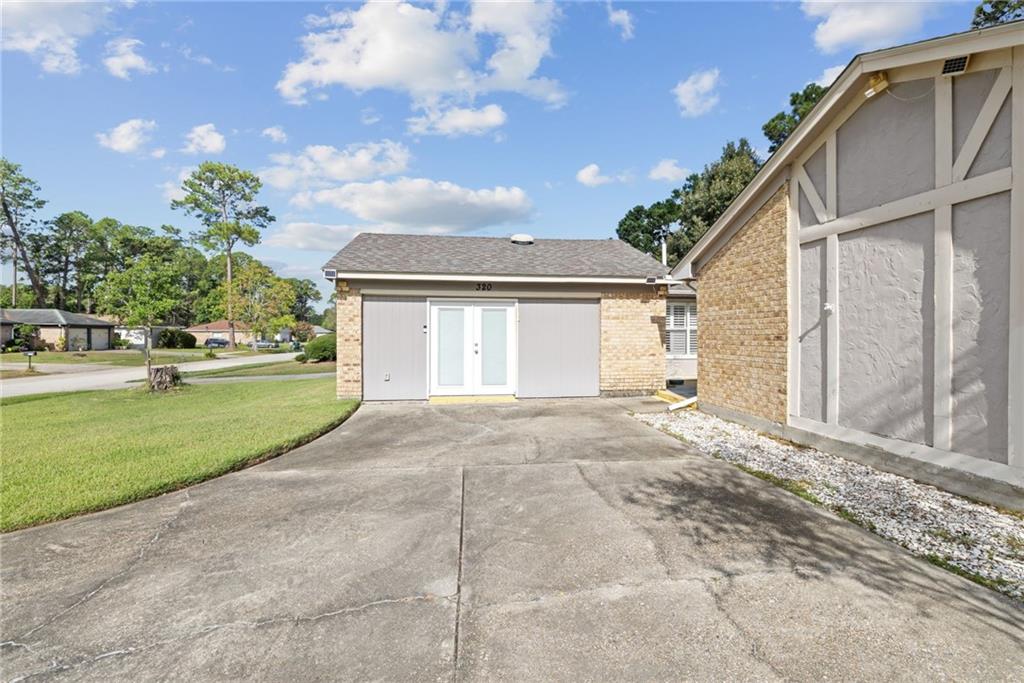Concrete driveway between brick outbuildings, with a white double entry door and lawn.