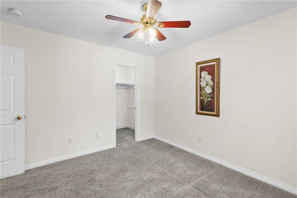 Empty bedroom with gray carpet, a ceiling fan, and an open closet.