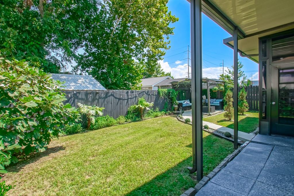 Backyard lawn bordered by mature trees and a privacy fence, with covered patio seating.
