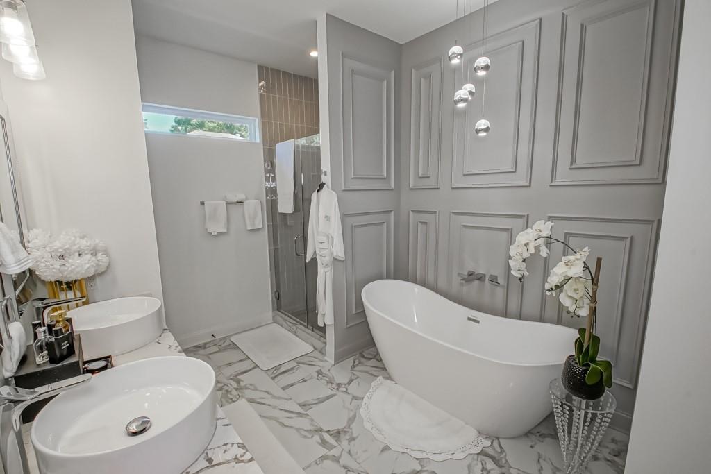 Modern bathroom with a freestanding soaking tub, glass shower, marble-patterned floor, and vessel sinks.