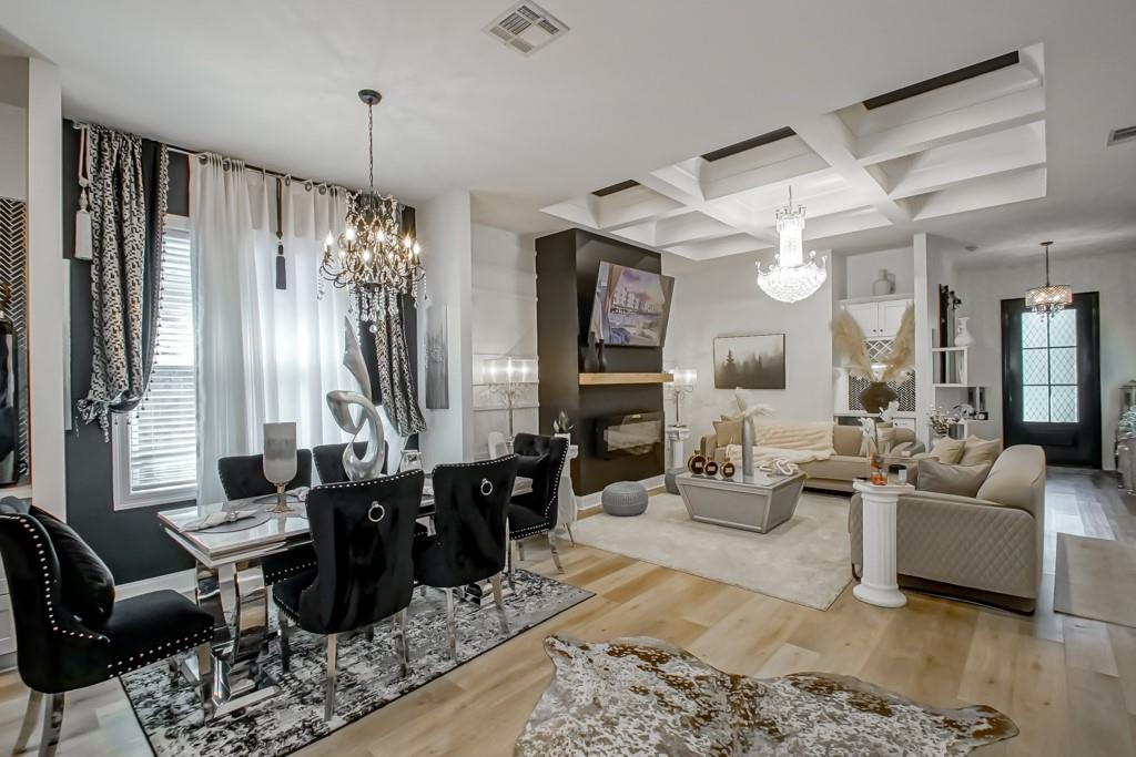 Open-plan living and dining room with a black fireplace, coffered ceiling, and crystal chandeliers.
