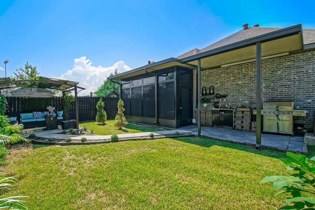 Backyard with a covered outdoor kitchen, grill, pergola seating area, and green lawn.