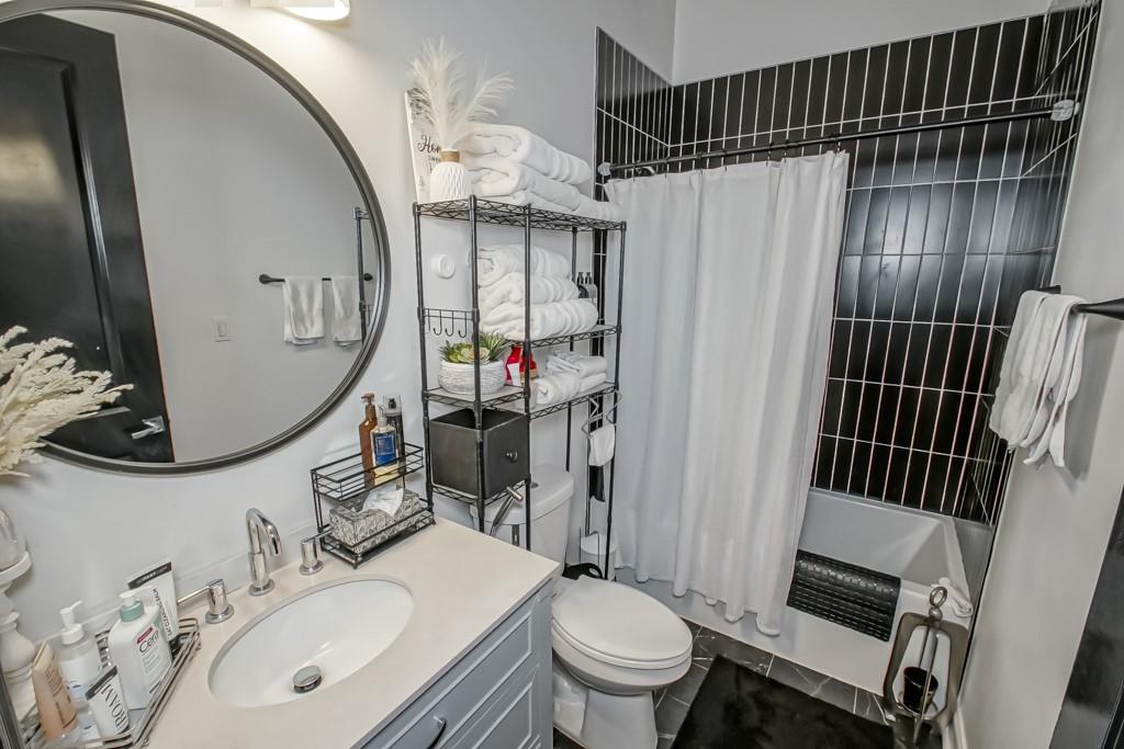Bathroom with a round mirror, white vanity, towel shelves, and black-tiled tub surround.