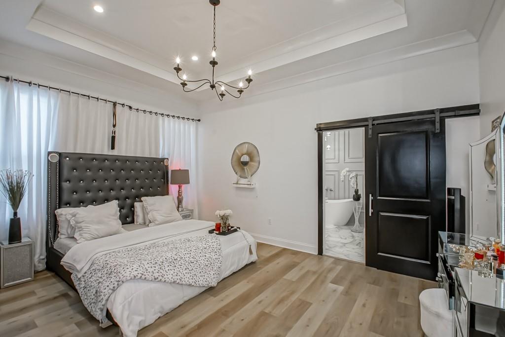 Bedroom with a tall black tufted headboard, white bedding, and an open barn door to the bathroom.