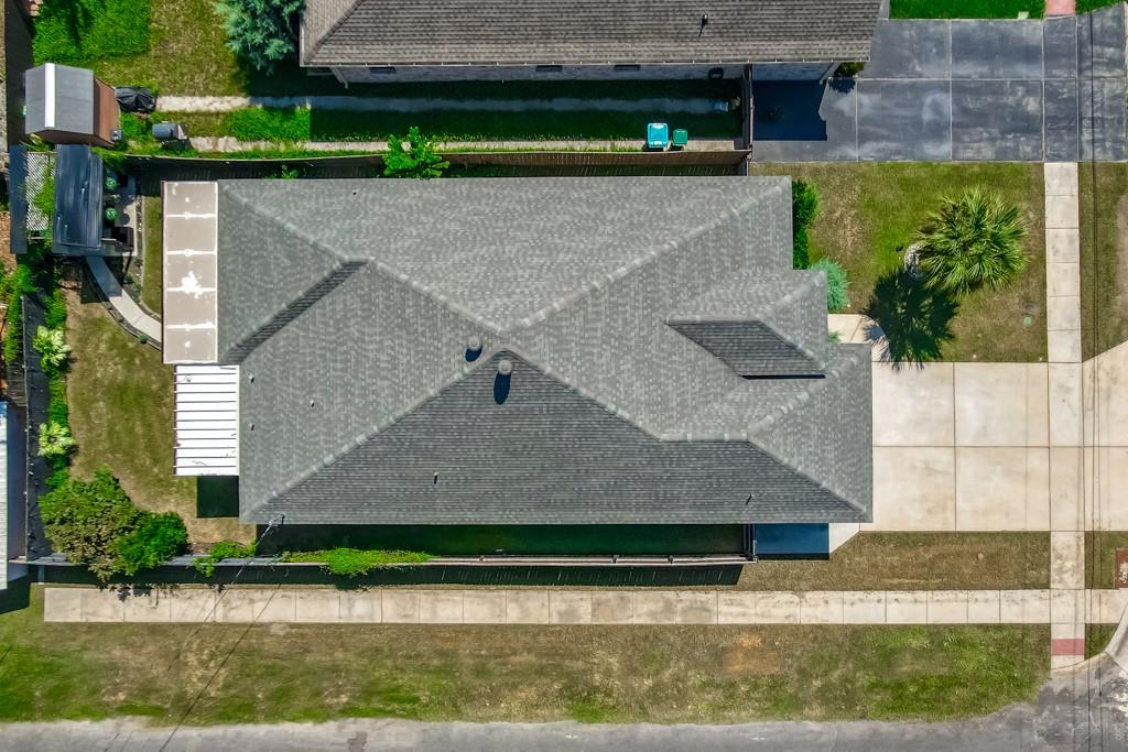 Aerial view of a gray-roofed house, surrounding lawn, sidewalks, and neighboring property.