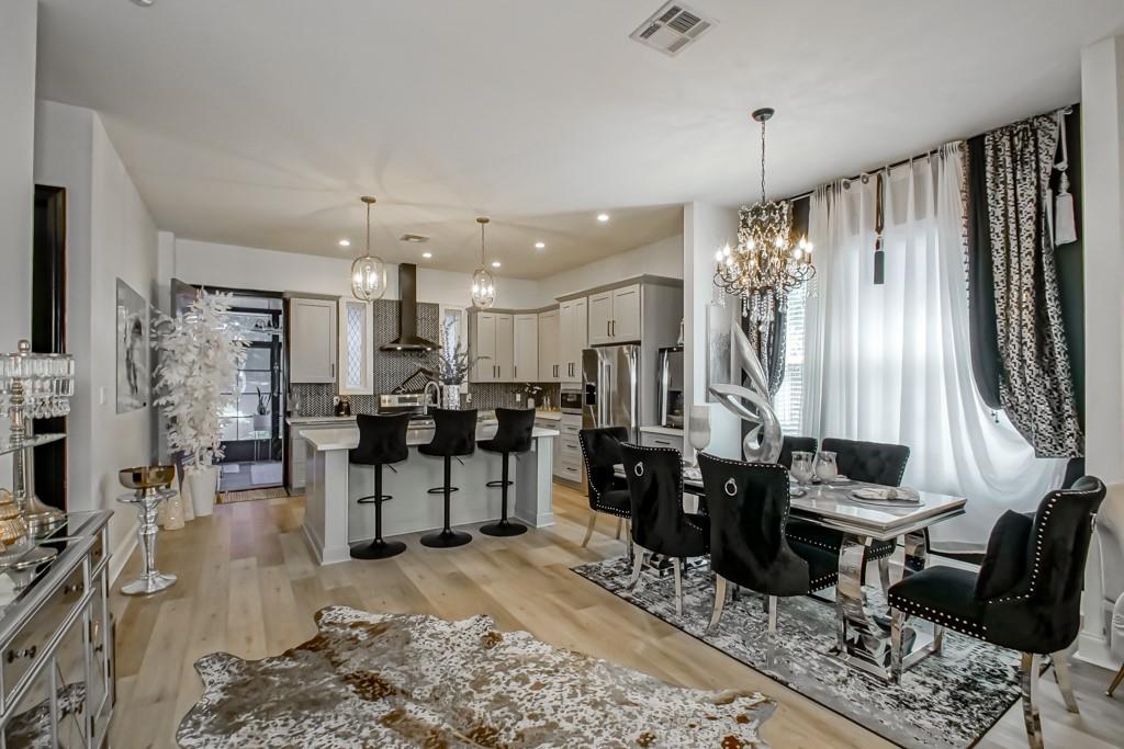 Open-plan kitchen and dining area with a white island, black bar stools, and chandelier-lit dining table.