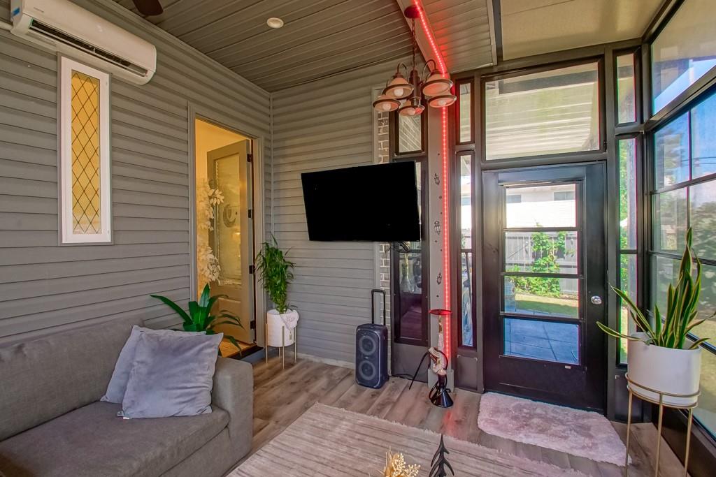 Furnished sunroom with a gray sofa, wall-mounted TV, and large windows beside a glass entry door.