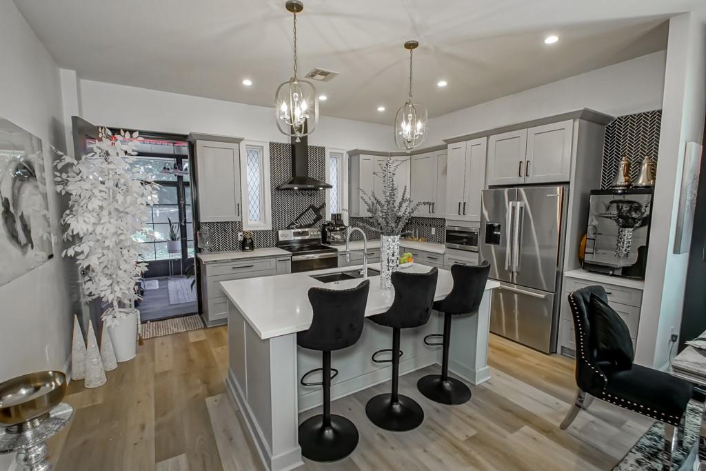 Kitchen with a large white island, three bar stools, gray cabinetry, and black patterned backsplashes.
