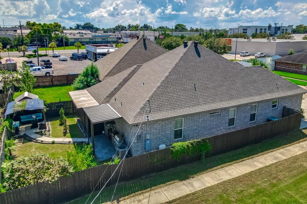 Aerial view of a gray-brick home with a large roof and fenced yard.
