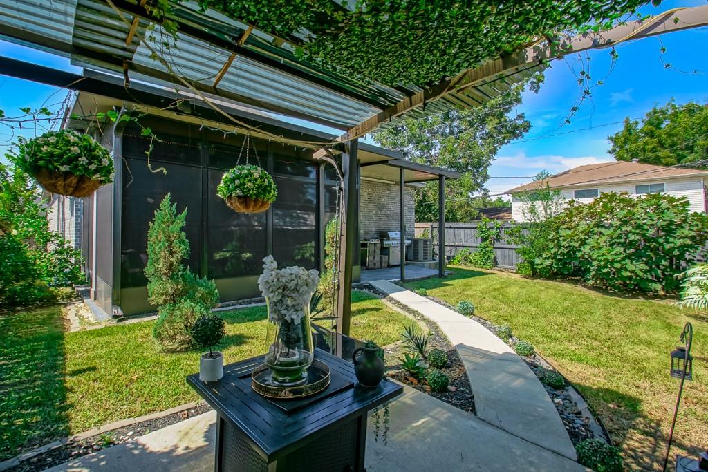 Backyard patio with a covered pergola, hanging plants, screened enclosure, and curved walkway through the lawn.